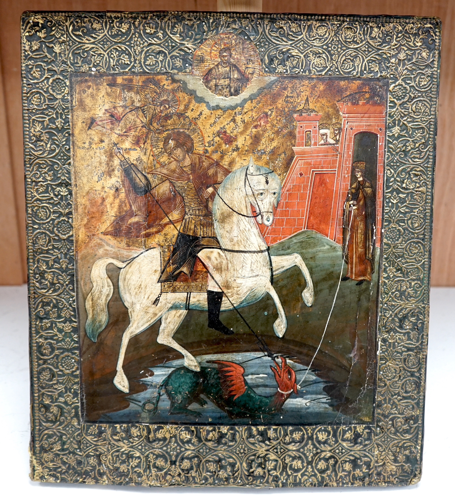 19th century Russian school, Icon, St George and The Dragon with Christ in Majesty above, applied stamped brass border, 45 x 37cm